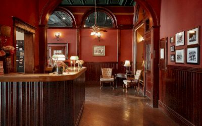 A cozy reception area with a wooden desk, elegant chairs, vintage decor, ambient lighting, and framed pictures on a red wall, creating a warm atmosphere.